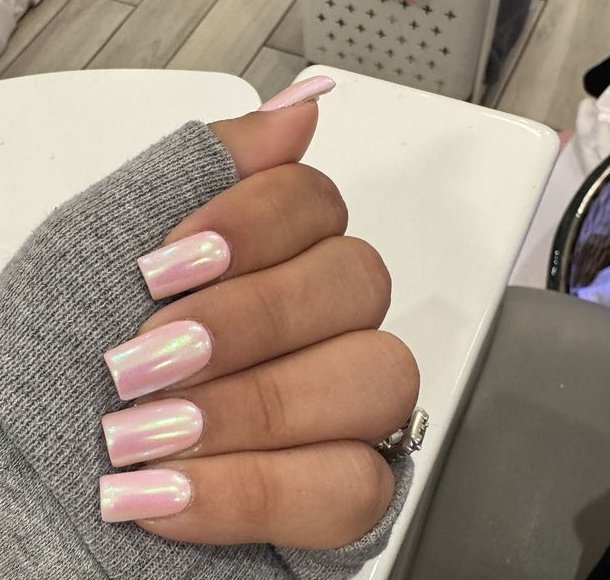 Iridescent pink square nails over a white manicure table in the salon