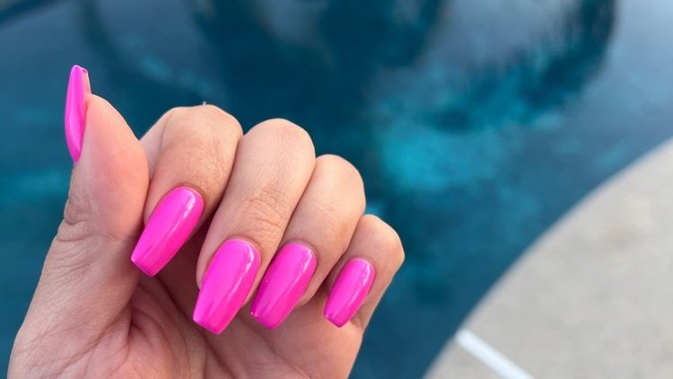 Hot pink coffin-shape nails held up over a backyard pool