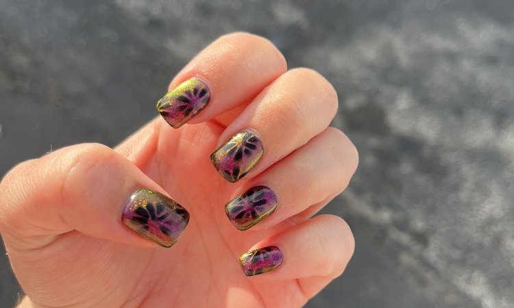 Short square nails in shifting purple and gold cat-eye polish with a dark flower design