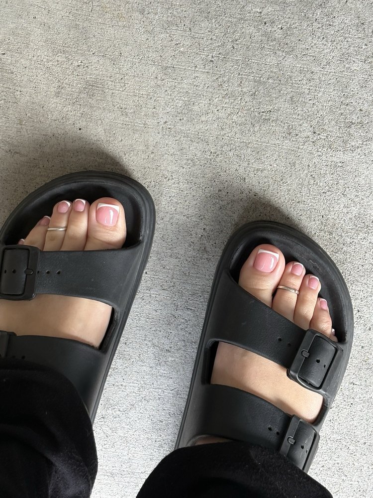 Pedicure with pink polish and white French tips, feet in black sandals