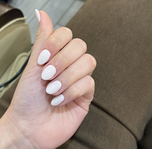 Short oval nails in glossy milky white, hand resting on a brown pedicure chair